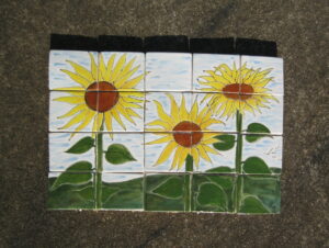 Porcelain tile mosaic, glazed with image of sunflowers in green grass background.